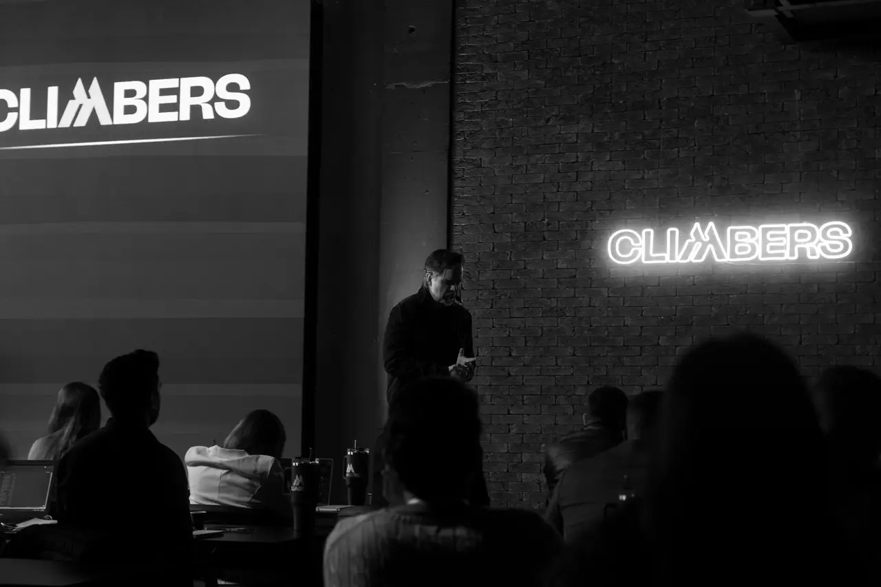 Plateia assiste à palestra com o neon Climbers na parede