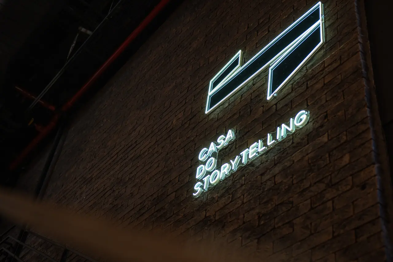 Logo da Casa do Storytelling em neon na parede de tijolos